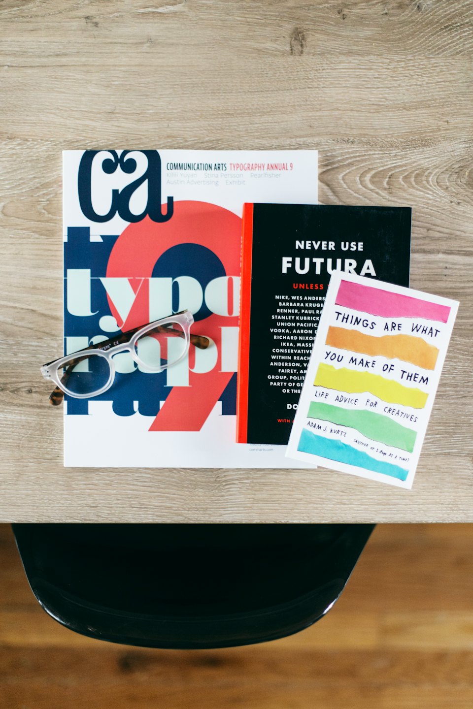 Magazines, postcard, and eyeglasses on a wooden table.
