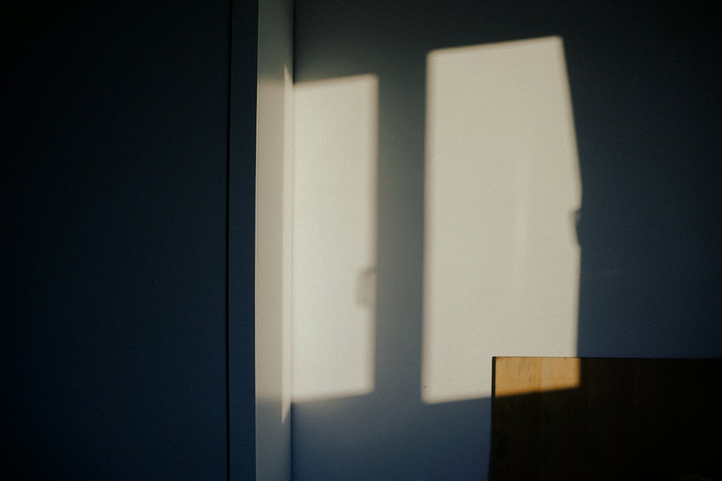 Sunlight creates geometric shapes on a light wall and dark wall.